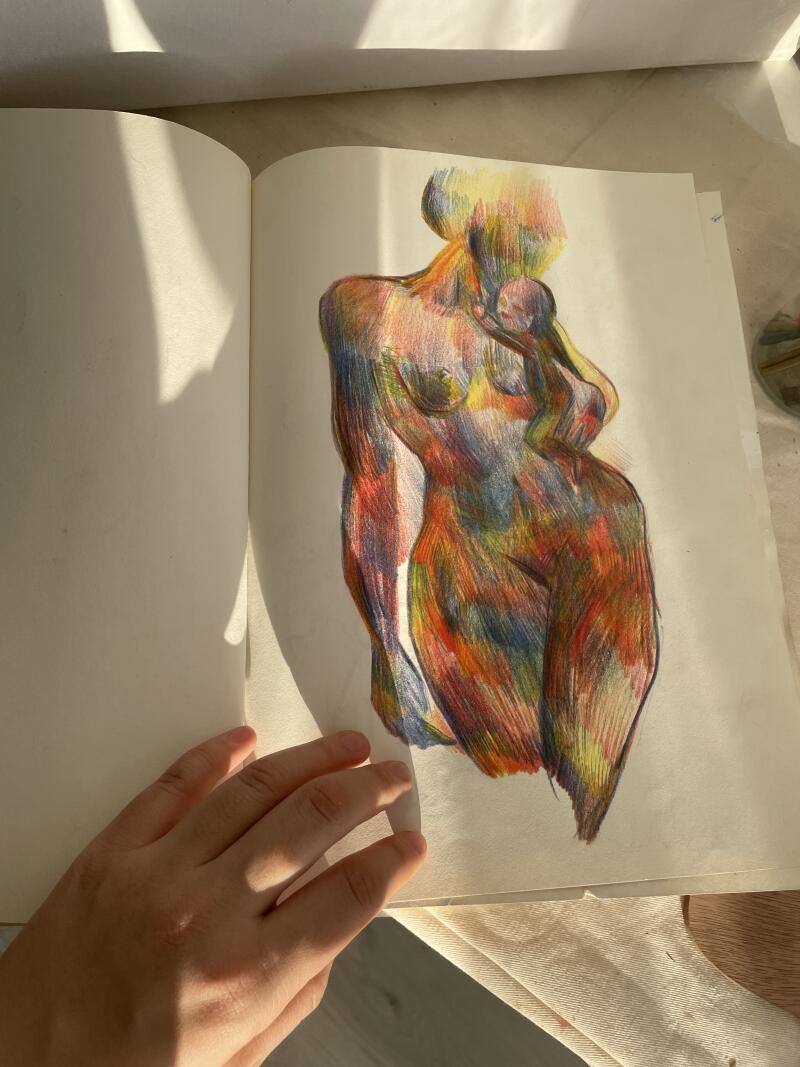 На развороте открытого альбома для набросков виден красочный рисунок женщины, держащей ребенка; на переднем плане видна рука.