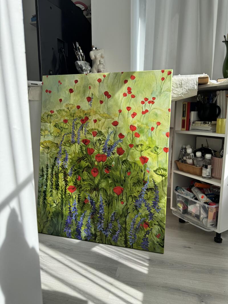 Картина с красными маками и фиолетовыми цветами на зеленом фоне прислонена к стене рядом с белой полкой.