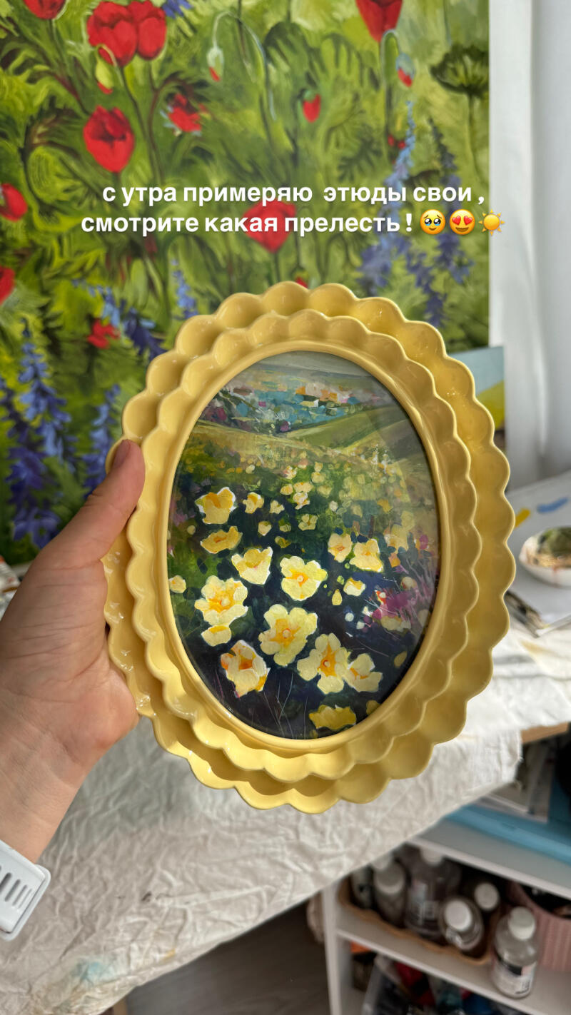 Рука держит небольшую картину в рамке с изображением желтых цветов в поле на фоне другой картины с красными и зелеными оттенками; текст на изображении гласит: «С утра примеряю этюды свои, смотрите какая прелесть!»