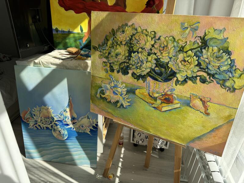 На изображении три картины: одна с цветами в вазе с морскими ракушками, одна с морскими ракушками на голубом фоне и еще одна с пейзажем в желто-зеленых тонах.