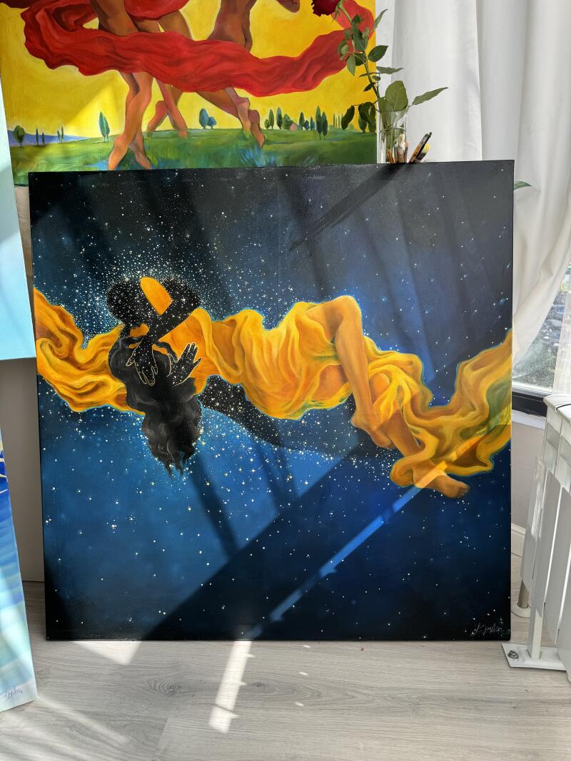 На изображении представлена картина маслом, на которой изображена фигура в развевающемся желтом платье на фоне темно-синего, усыпанного звездами неба, создающая небесный эффект, с силуэтом другой фигуры в центре, и она размещена перед другой картиной и окном.