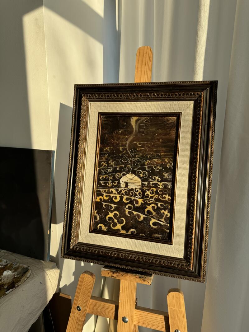 На картине в раме, стоящей на деревянном мольберте, изображена юрта с дымом, поднимающимся из ее вершины, на темном фоне с витиеватыми узорами.