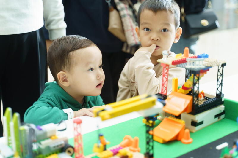 Двое маленьких детей играют с тематическим набором Lego на тему строительства, в котором есть краны и строительное оборудование.