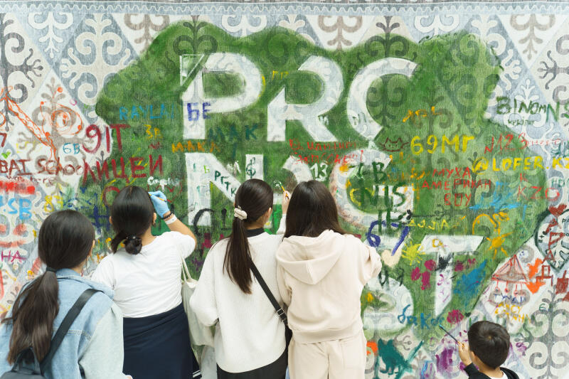 Несколько человек рисуют на стене с текстом «PRC» и другими словами разных цветов.