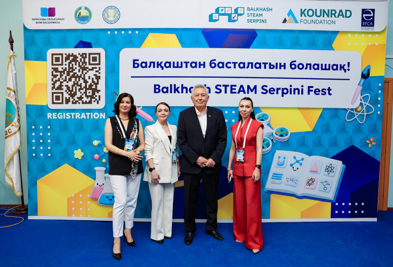 Four people stand in front of a backdrop that reads "Балқаштан басталатын болашақ! Balkhash STEAM Serpini Fest". The backdrop also features a QR code labeled "REGISTRATION" and logos for BALKHASH STEAM SERPINI, KOUNRAD FOUNDATION, and EFCA.