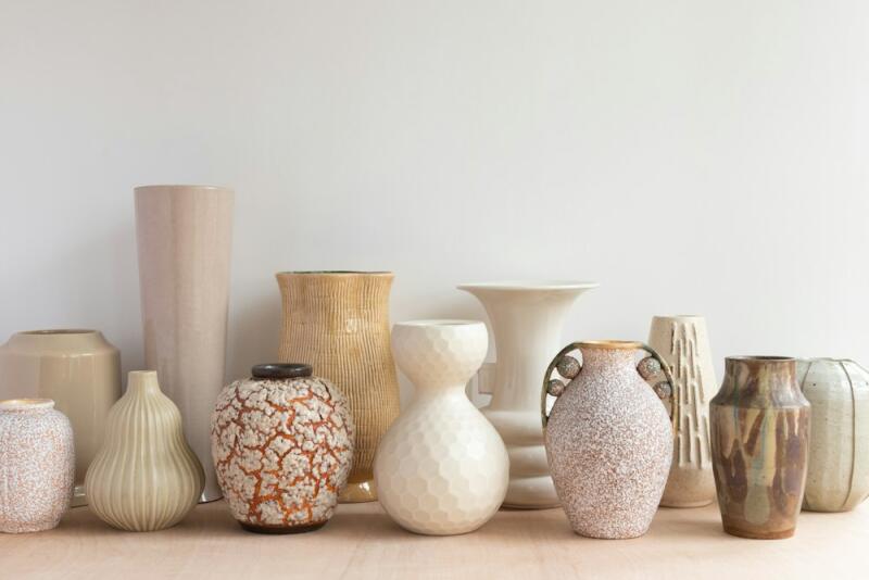 A diverse collection of ceramic vases in various shapes, sizes, and earthy tones, featuring different textures like ribbed, speckled, crackle glaze, and honeycomb patterns, arranged on a light surface against a white background.
