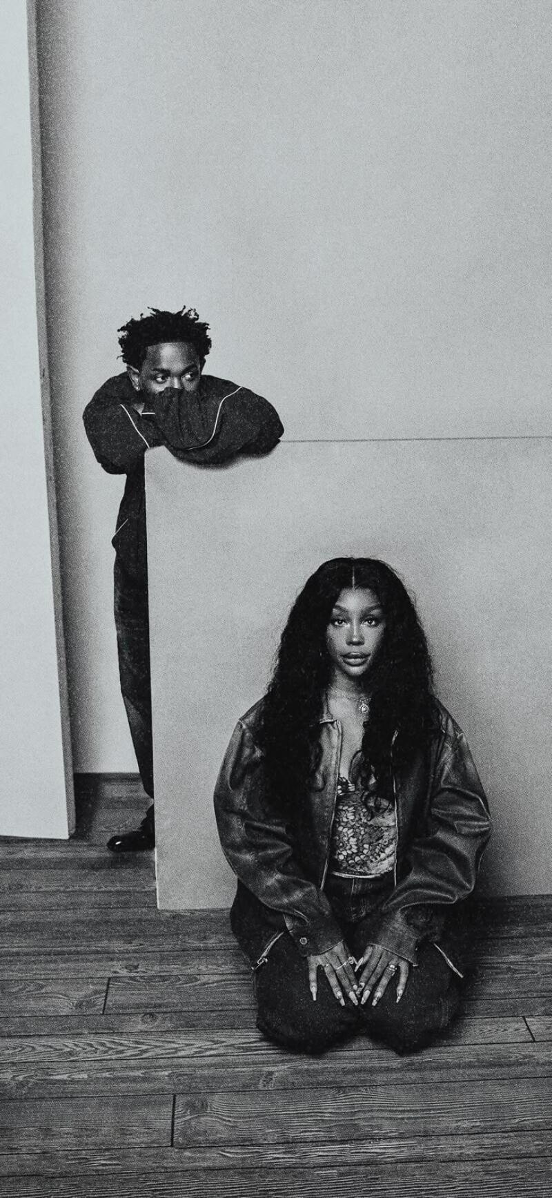 A grayscale portrait features a woman kneeling in the foreground, wearing a jacket over a patterned top, with a man partially visible behind a partition in the background.