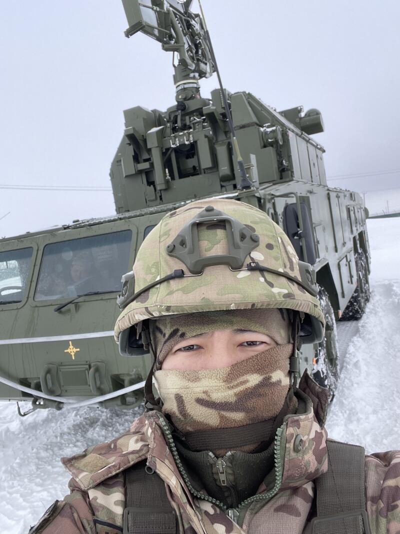 Солдат в камуфляже стоит перед военной техникой, покрытой снегом.