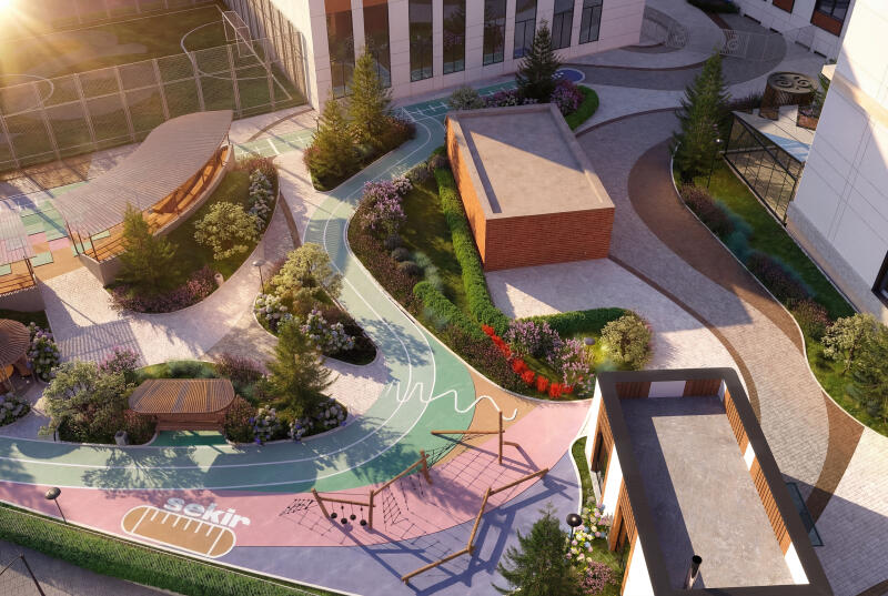 This aerial view shows a colorful playground with a running track, climbing structures, and various seating areas surrounded by landscaping and buildings; the word "sekir" is visible on the ground.
