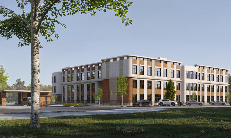 The image shows a modern, multi-story building with a mix of beige and brick facade, surrounded by green lawns and trees, with several cars parked in front.
