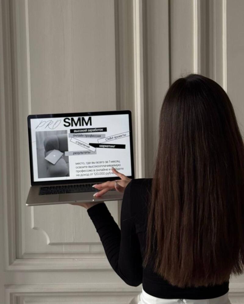 A woman with long brown hair holds a laptop displaying the text "PRO SMM", along with other text in Russian advertising a high-paying online profession and SMM projects.