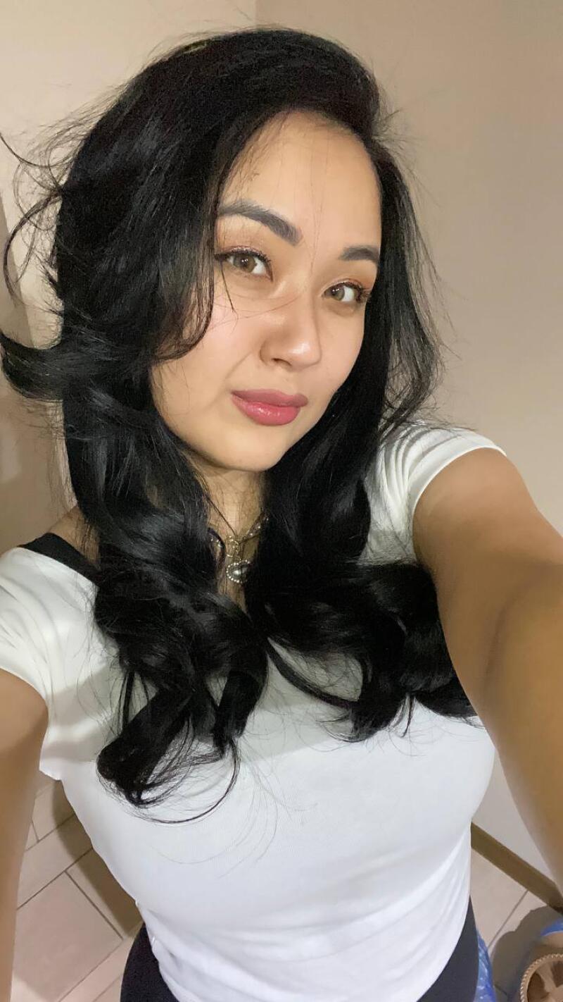 A selfie of a woman with dark hair and brown eyes wearing a white shirt and a necklace.