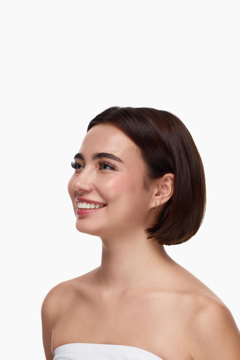 A woman with short, dark hair and a white strapless top smiles and looks to the side.