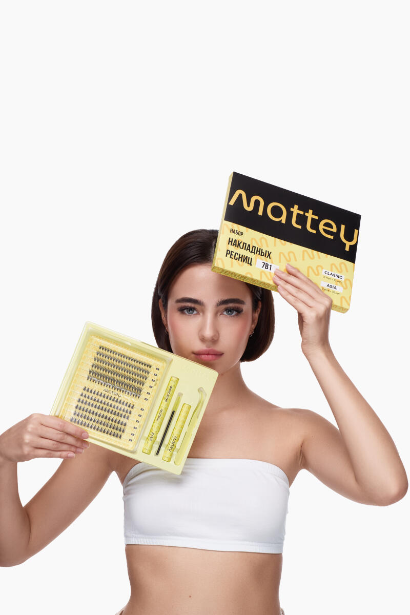 A fair-skinned woman in a white tube top holds a Mattey eyelash set and an open kit, displaying the individual lashes and tools, against a plain white background.
