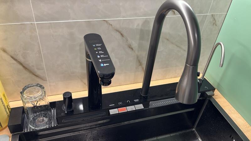 A modern kitchen area with a black sink, a black faucet featuring a digital display (showing "88°", "55%", "60%", "100%", "Кипяток", "Охлажд", "Вода"), a separate silver filtered water tap, and control buttons, all set on a wooden countertop with a tiled backsplash.