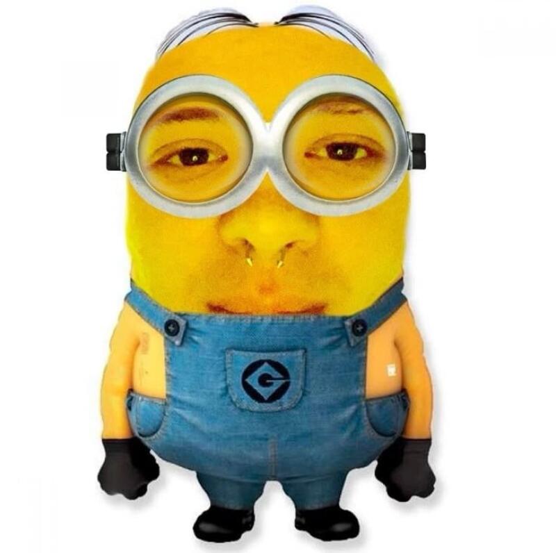 A yellow, Minion-like character with a human face, wearing silver goggles, blue denim overalls with a 'G' logo, and black gloves and shoes, standing against a white background. The human face features visible eyes, a nose with a septum ring, and a mouth.