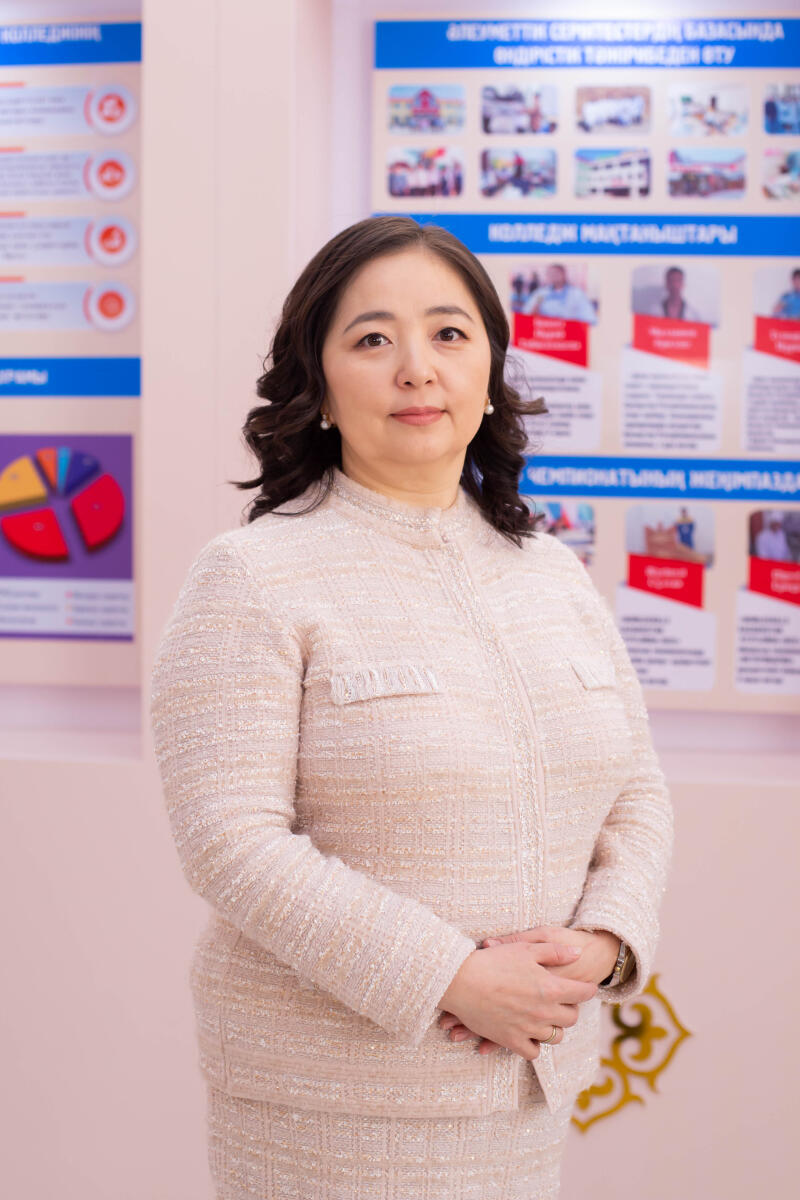 A woman with dark, wavy hair and pearl earrings stands in a light beige tweed suit, with her hands clasped. In the background, there are informational posters on light pink walls and a yellow ornamental pattern.