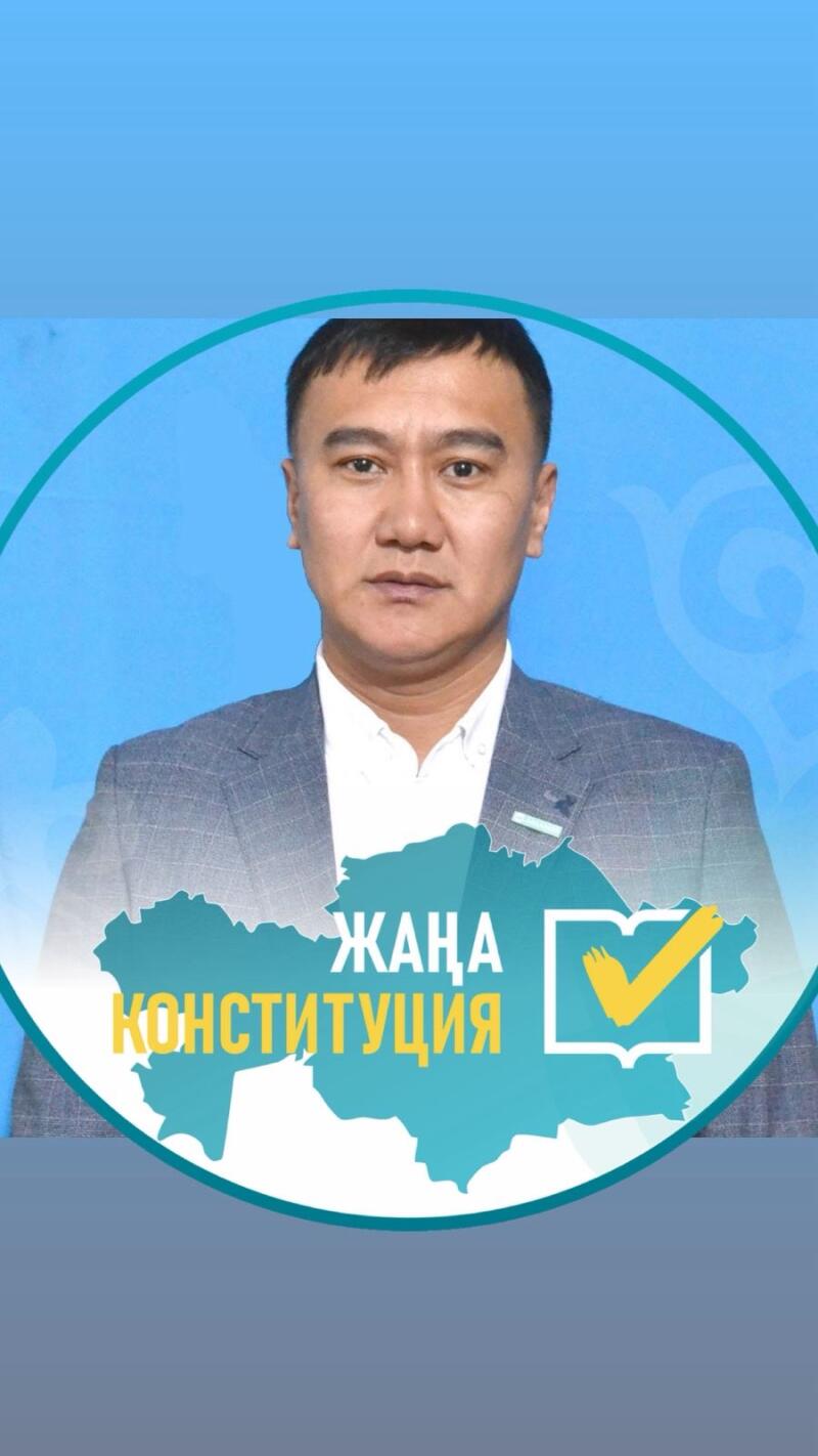 A man in a grey suit and white shirt is centered on a blue background, framed by a light blue circle. Below him is a turquoise map shape with yellow text "ЖАҢА КОНСТИТУЦИЯ" (NEW CONSTITUTION) and a yellow checkmark icon.