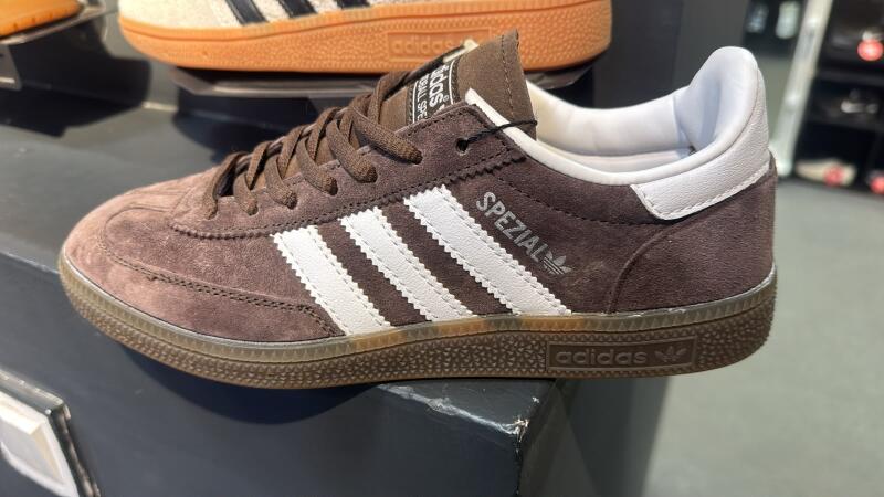 A brown suede Adidas sneaker with white stripes and "SPEZIAL" text on the side, and an "adidas" logo visible on the dark brown sole.