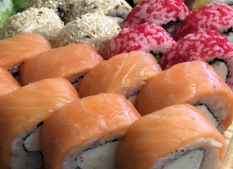 A close-up view of an assortment of sushi rolls, featuring salmon-wrapped rolls, rolls topped with white sesame seeds, and rolls with red roe.