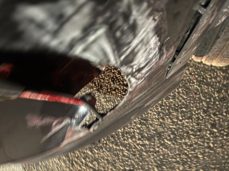 A close-up, blurry view of a torn dark bag revealing brown pellets inside, with a red strap visible and the bag resting on a textured ground.