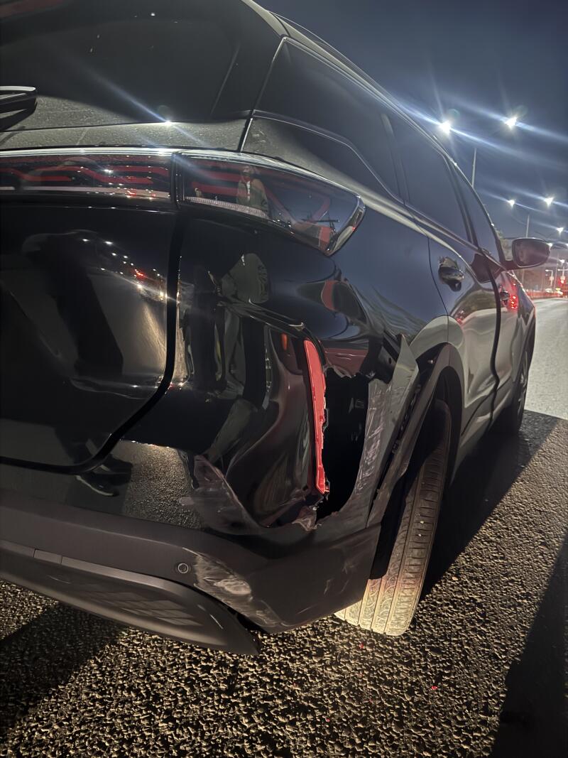 The rear-right side of a black car is shown at night with significant damage to the fender and bumper, including a broken taillight and dented bodywork.