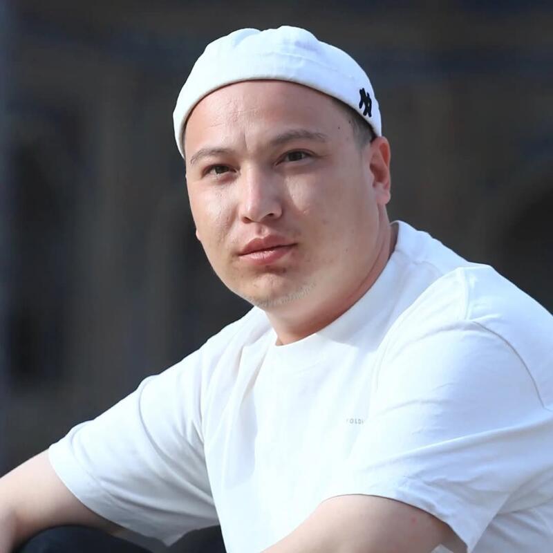 A man wearing a white t-shirt and a white cap with a black logo, looking directly at the camera.