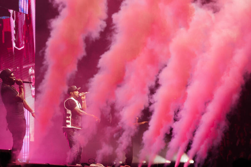 Two men are singing on stage with pink smoke surrounding them.