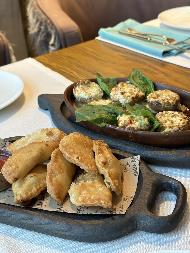 The image shows two dark wooden trays with food: one with fried pastries and the other with stuffed mushrooms and spinach.