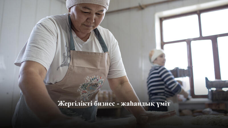 Женщина в фартуке и головном уборе месит тесто, на заднем плане видна еще одна женщина; текст на изображении гласит: "Жергілікті бизнес - жаһандық үміт".