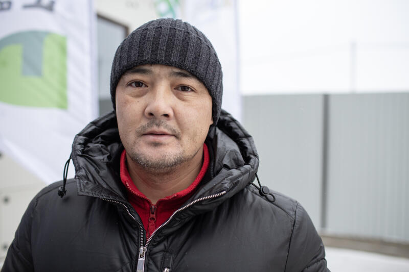 Мужчина средних лет в черной шапке и пуховике с красной майкой смотрит прямо в камеру.