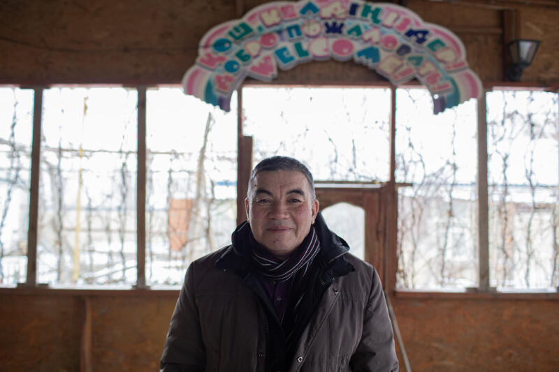 Мужчина стоит перед окном с надписью "Добро пожаловать" на казахском и английском языках.